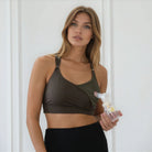 Woman holding a breast pump bottle against a white background, featuring sweat and milk's high impact nursing and pumping sports bra in dark cactus