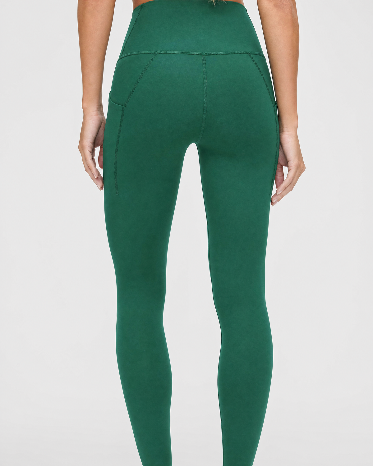 A person shown from the back wearing dark green / pine green high-waisted leggings against a light gray studio background.