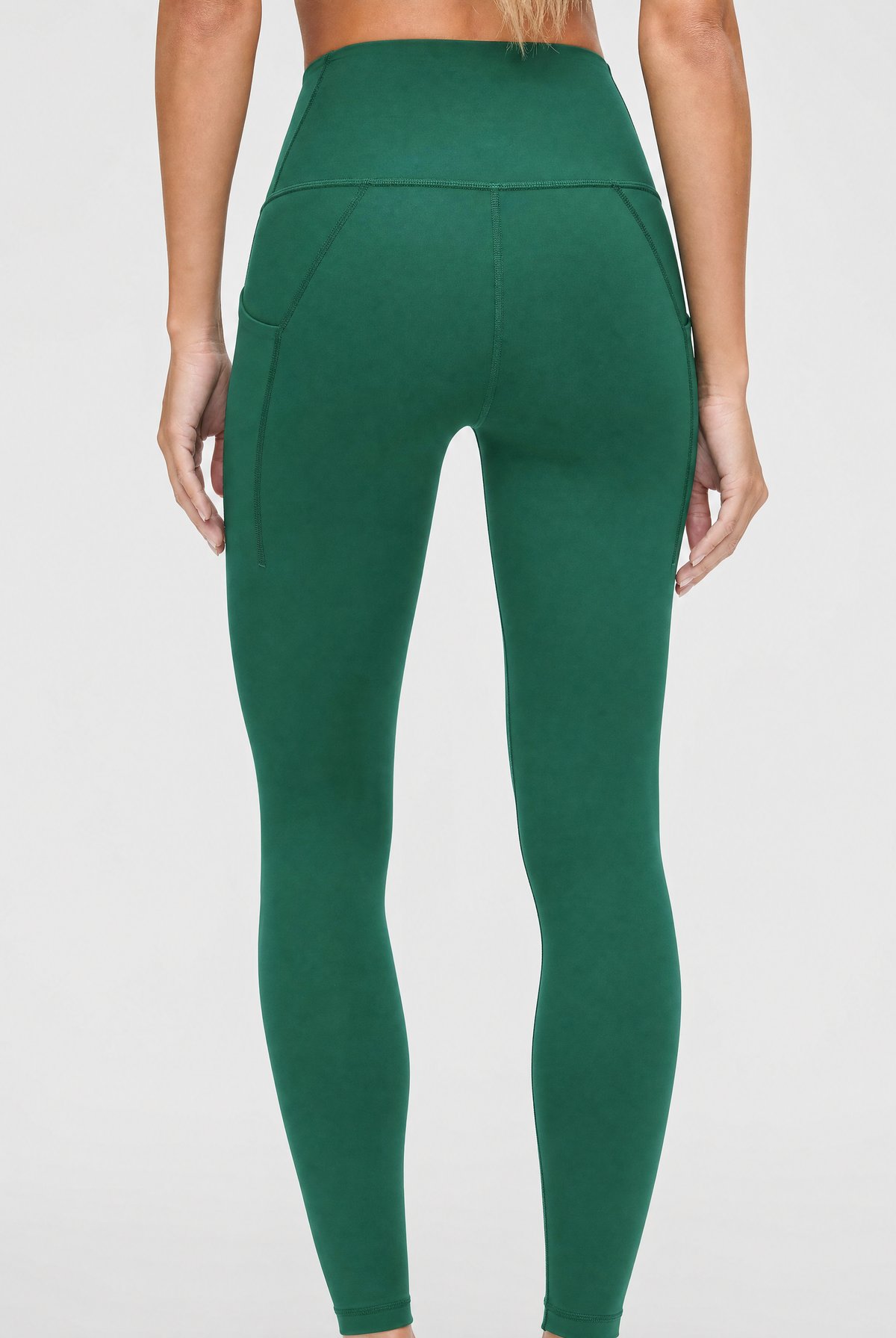 A person shown from the back wearing dark green / pine green high-waisted leggings against a light gray studio background.