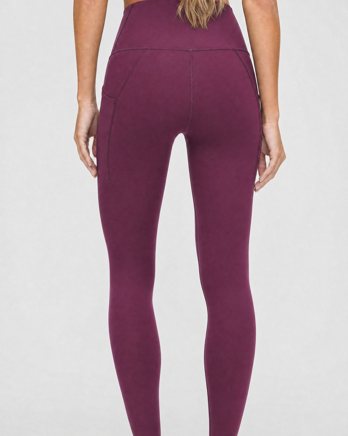A model wearing high-waisted, full-length postpartum leggings from sweat and milk in a deep plum purple color or bordeaux color shown from the waist down against a light gray studio background, back shot