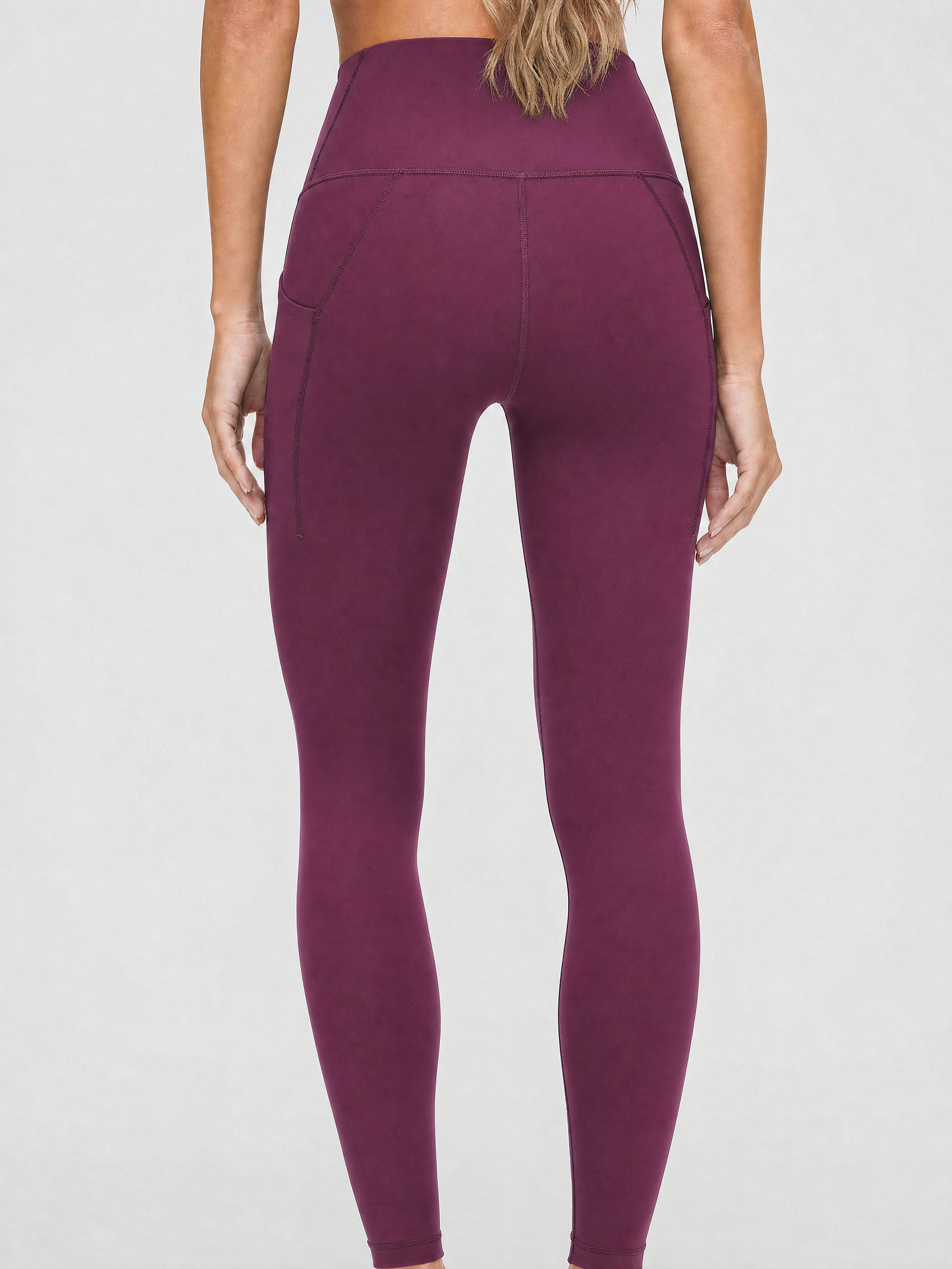 A model wearing high-waisted, full-length postpartum leggings from sweat and milk in a deep plum purple color or bordeaux color shown from the waist down against a light gray studio background, back shot
