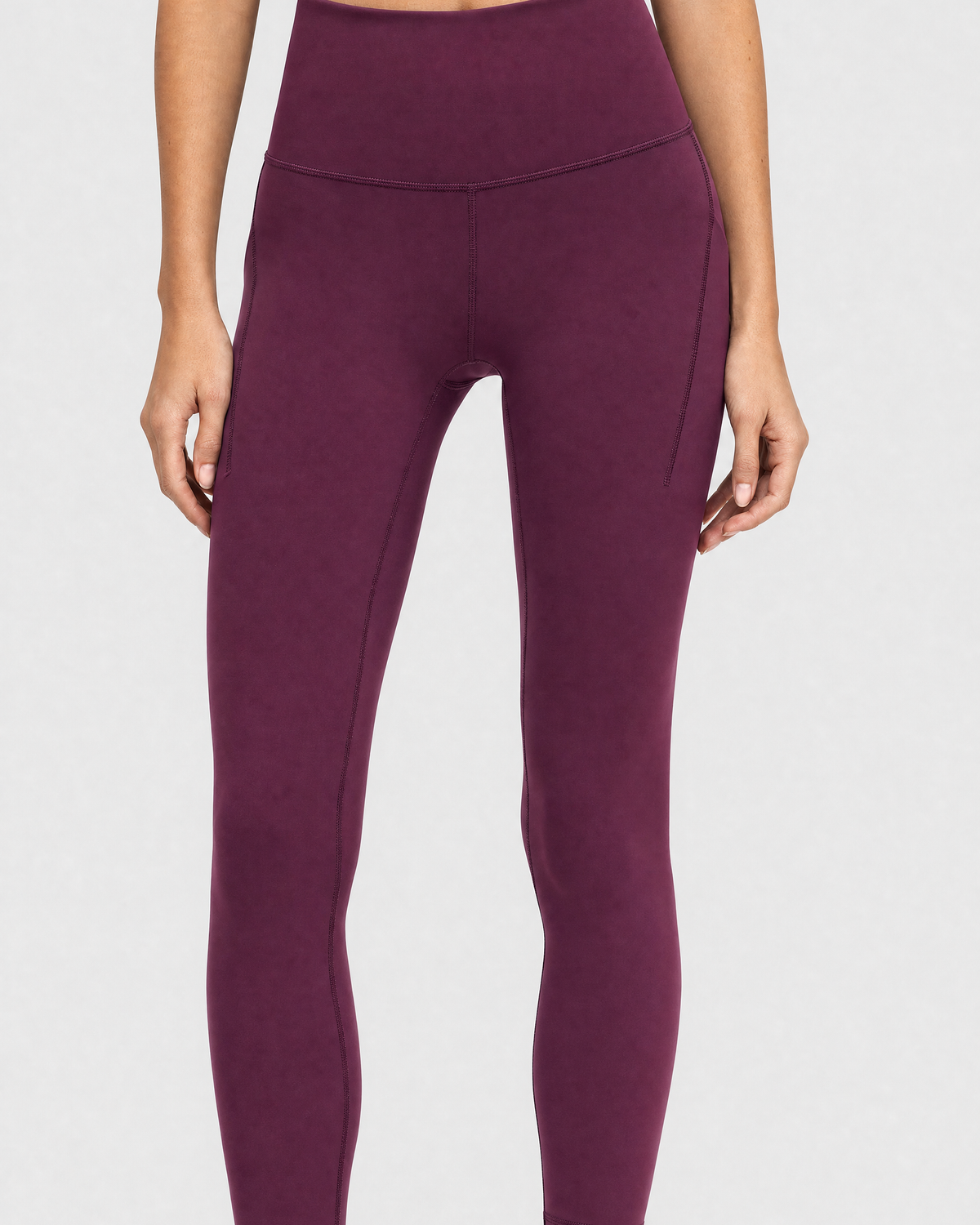 A model wearing high-waisted, full-length postpartum leggings from sweat and milk in a deep plum purple color or bordeaux color shown from the waist down against a light gray studio background.