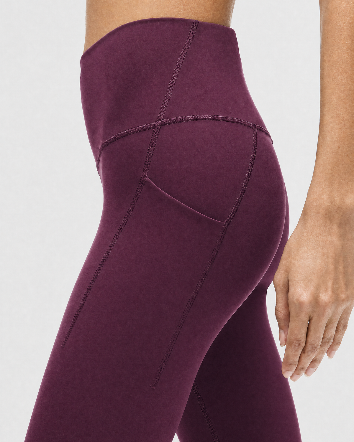 A model wearing high-waisted, full-length postpartum leggings from sweat and milk in a deep plum purple color or bordeaux color shown from the waist down against a light gray studio background, side shot