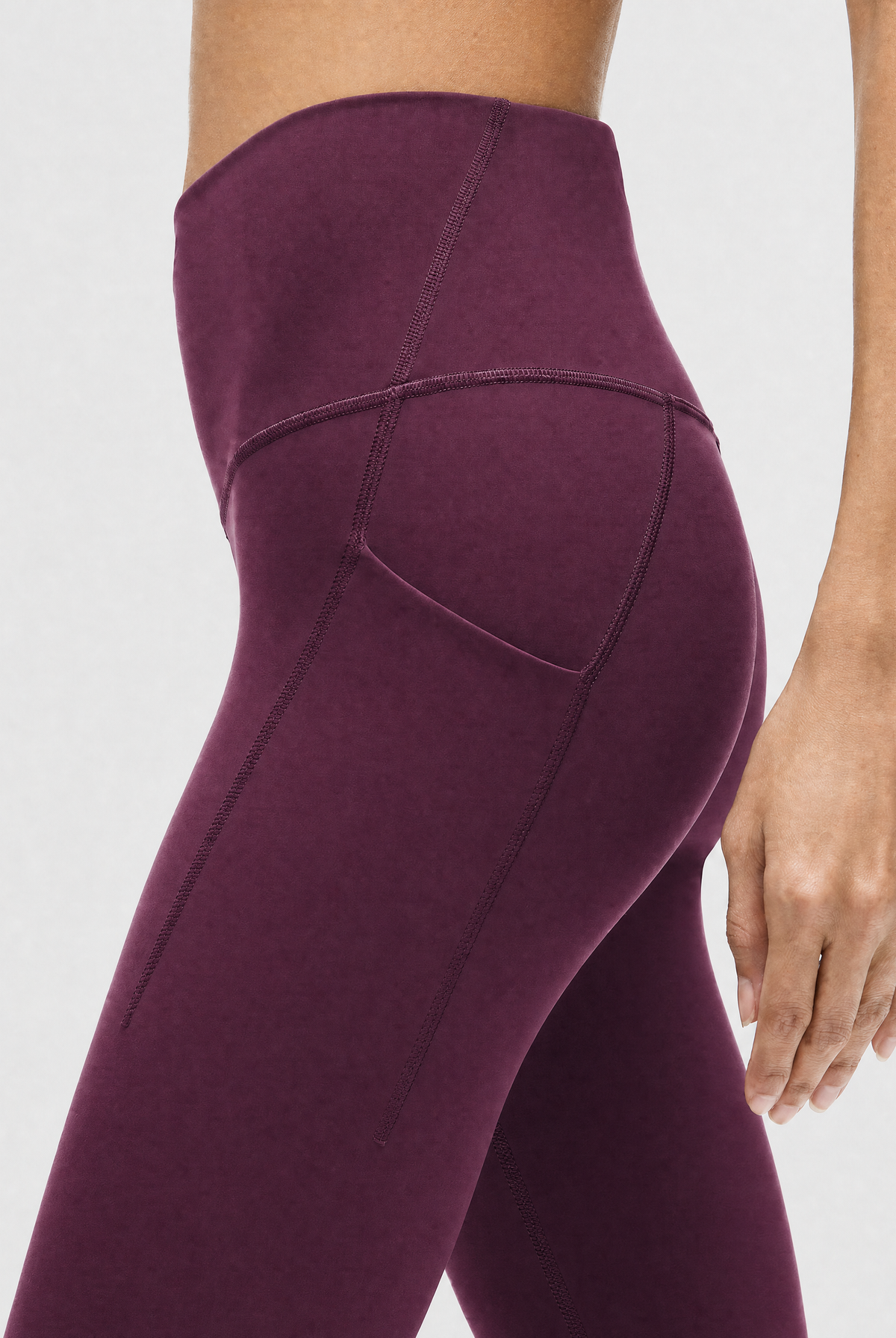 A model wearing high-waisted, full-length postpartum leggings from sweat and milk in a deep plum purple color or bordeaux color shown from the waist down against a light gray studio background, side shot