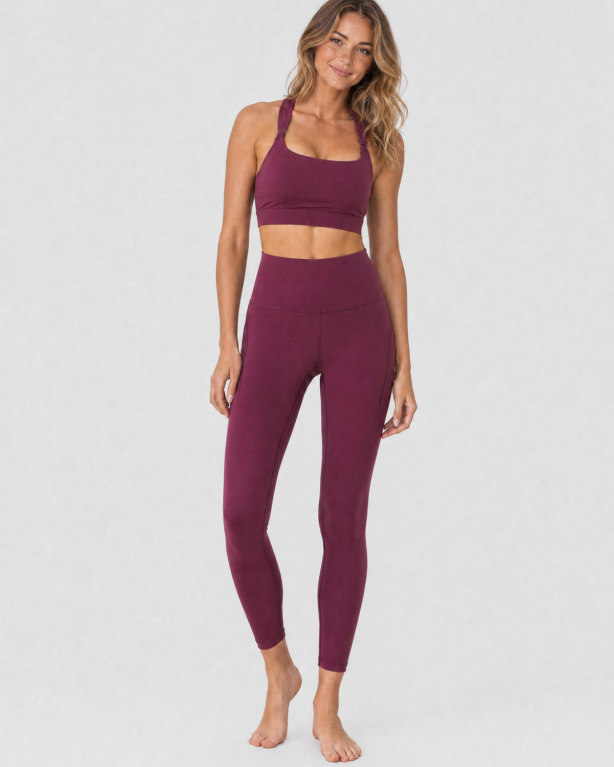A model wearing high-waisted, full-length postpartum leggings from sweat and milk in a deep plum purple color or bordeaux color shown from the waist down against a light gray studio background, full body shot