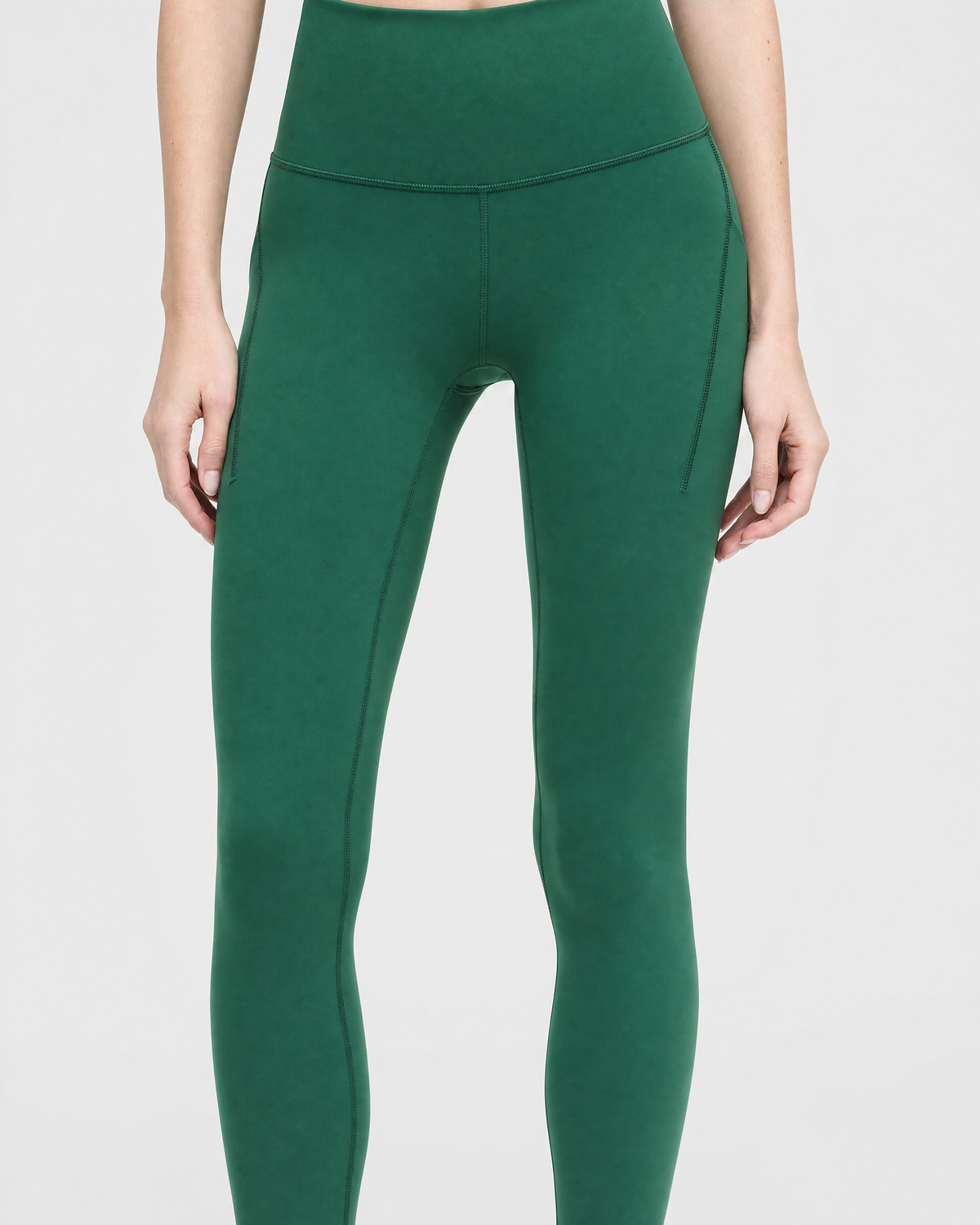 A model wearing high-waisted, full-length pine green leggings against a light gray studio background, front shot