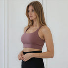 Woman wearing a sweat and milk high impact nursing and pumping Venice 3 mauve sports bra and black leggings against a white background