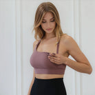 Woman wearing a mauve high impact nursing and pumping sports bra, folding down one side, and black leggings against a white background, from sweat and milk