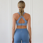 a woman wearing a sweat and milk's high impact Chloe 3 running nursing and pumping sports bra in tile blue, showing the beautiful back straps in crisscross style