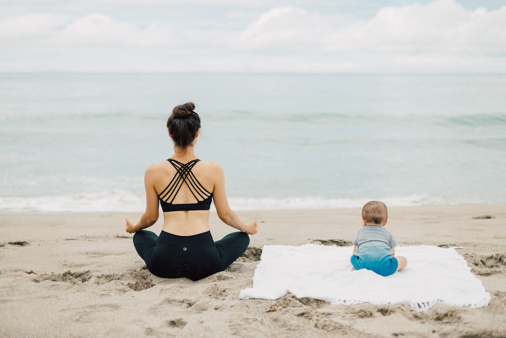 A new mom doing yoga with her baby on the Malibu beach in Sweat & Milk's nursing sports bra