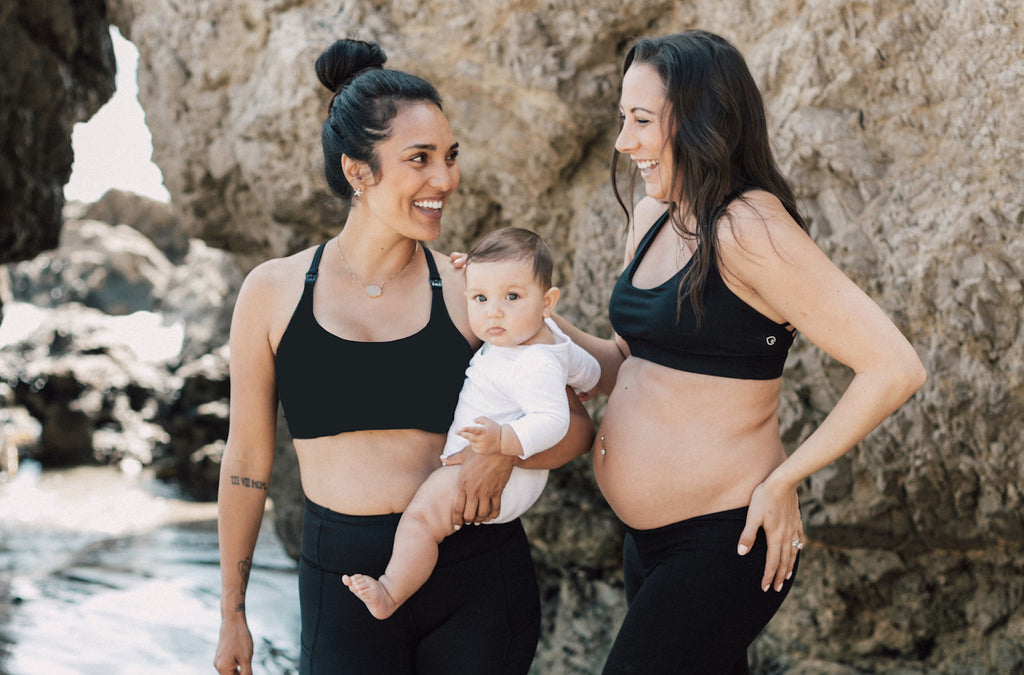  Two new moms wearing sweat and Milk's nursing bras playing with their babies on the Malibu beach