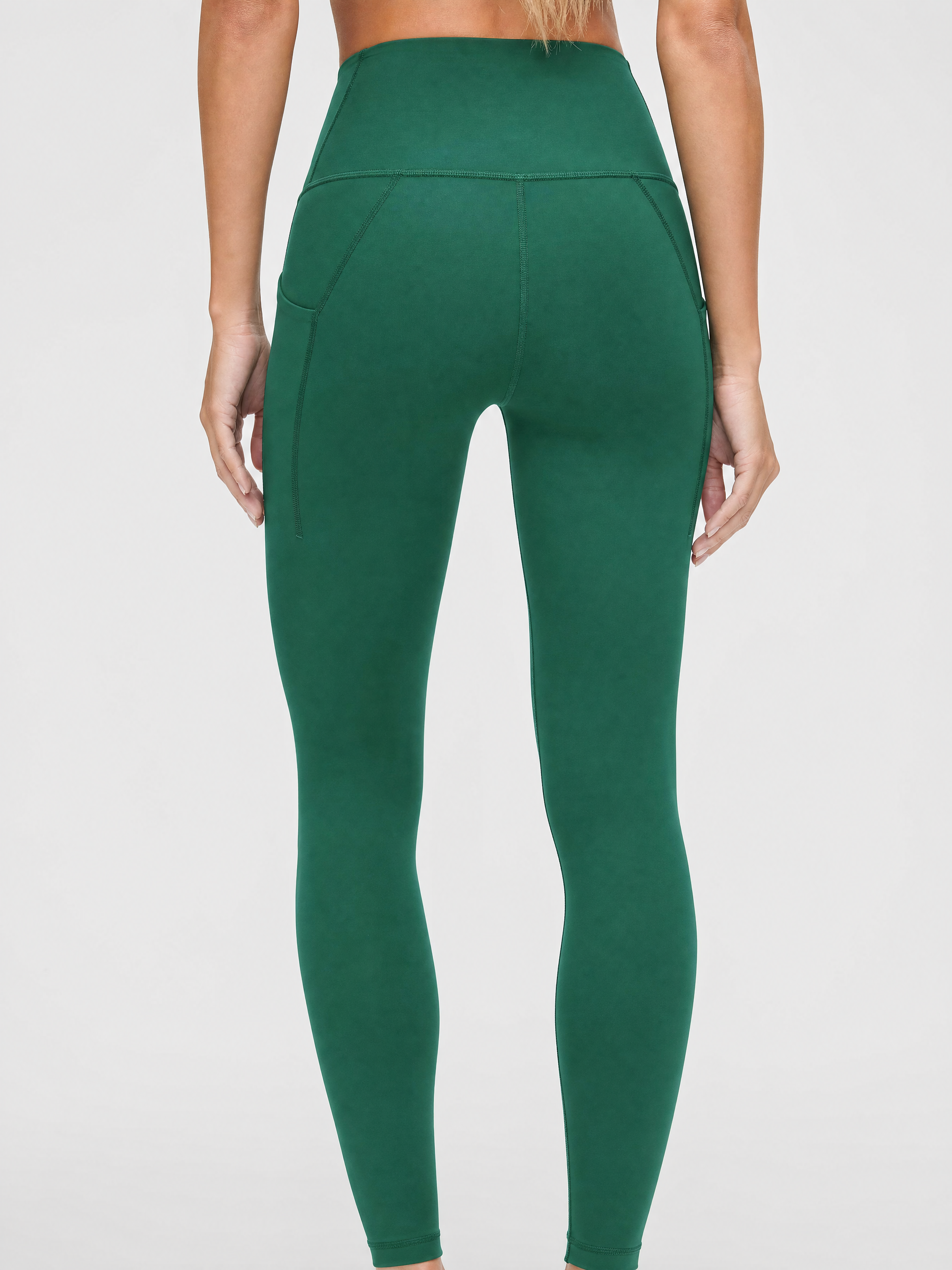 A person shown from the back wearing dark green / pine green high-waisted leggings against a light gray studio background.