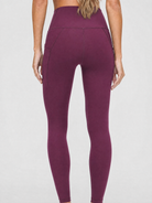 A model wearing high-waisted, full-length postpartum leggings from sweat and milk in a deep plum purple color or bordeaux color shown from the waist down against a light gray studio background, back shot