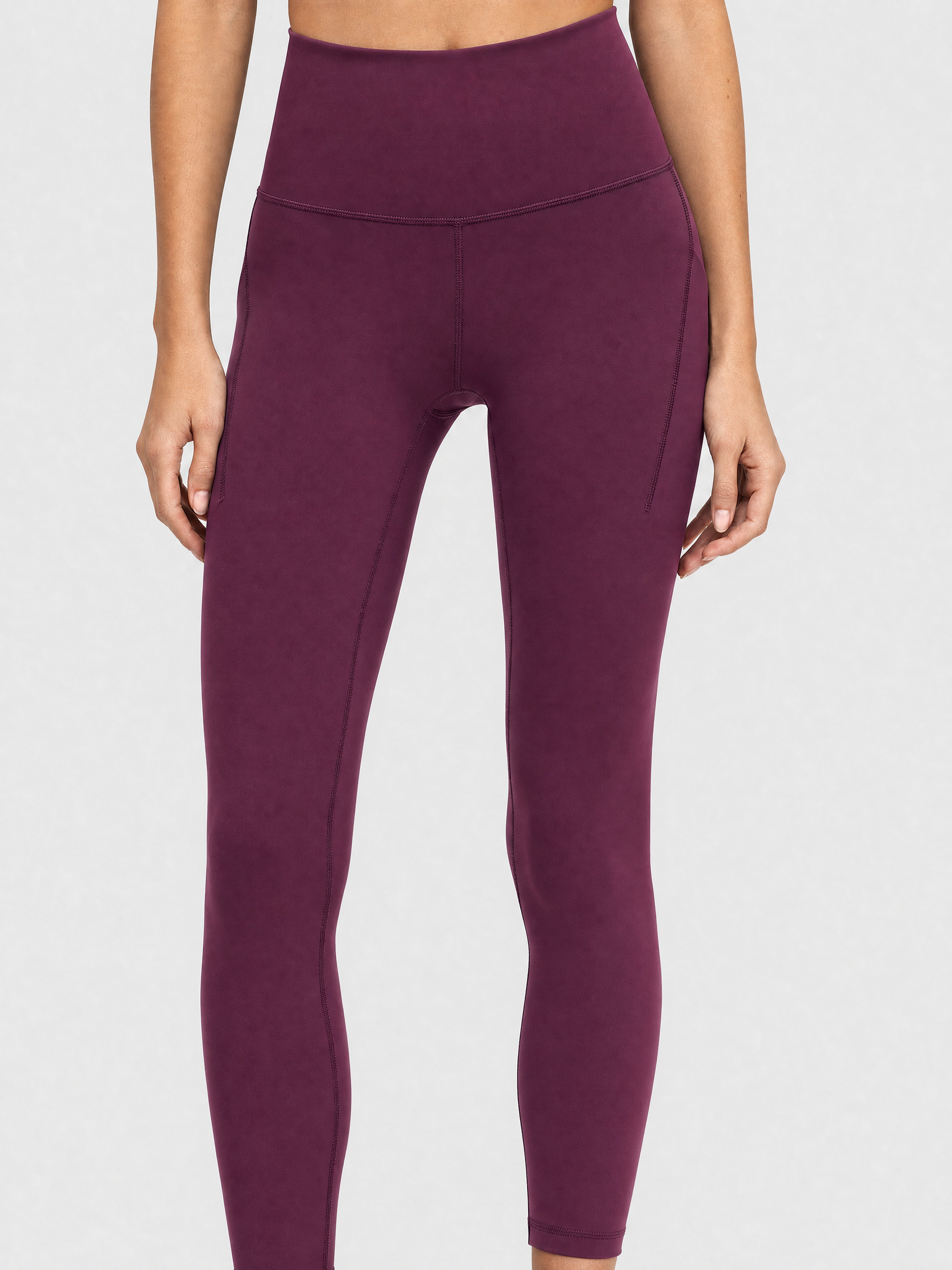 A model wearing high-waisted, full-length postpartum leggings from sweat and milk in a deep plum purple color or bordeaux color shown from the waist down against a light gray studio background.