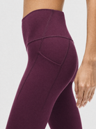 A model wearing high-waisted, full-length postpartum leggings from sweat and milk in a deep plum purple color or bordeaux color shown from the waist down against a light gray studio background, side shot