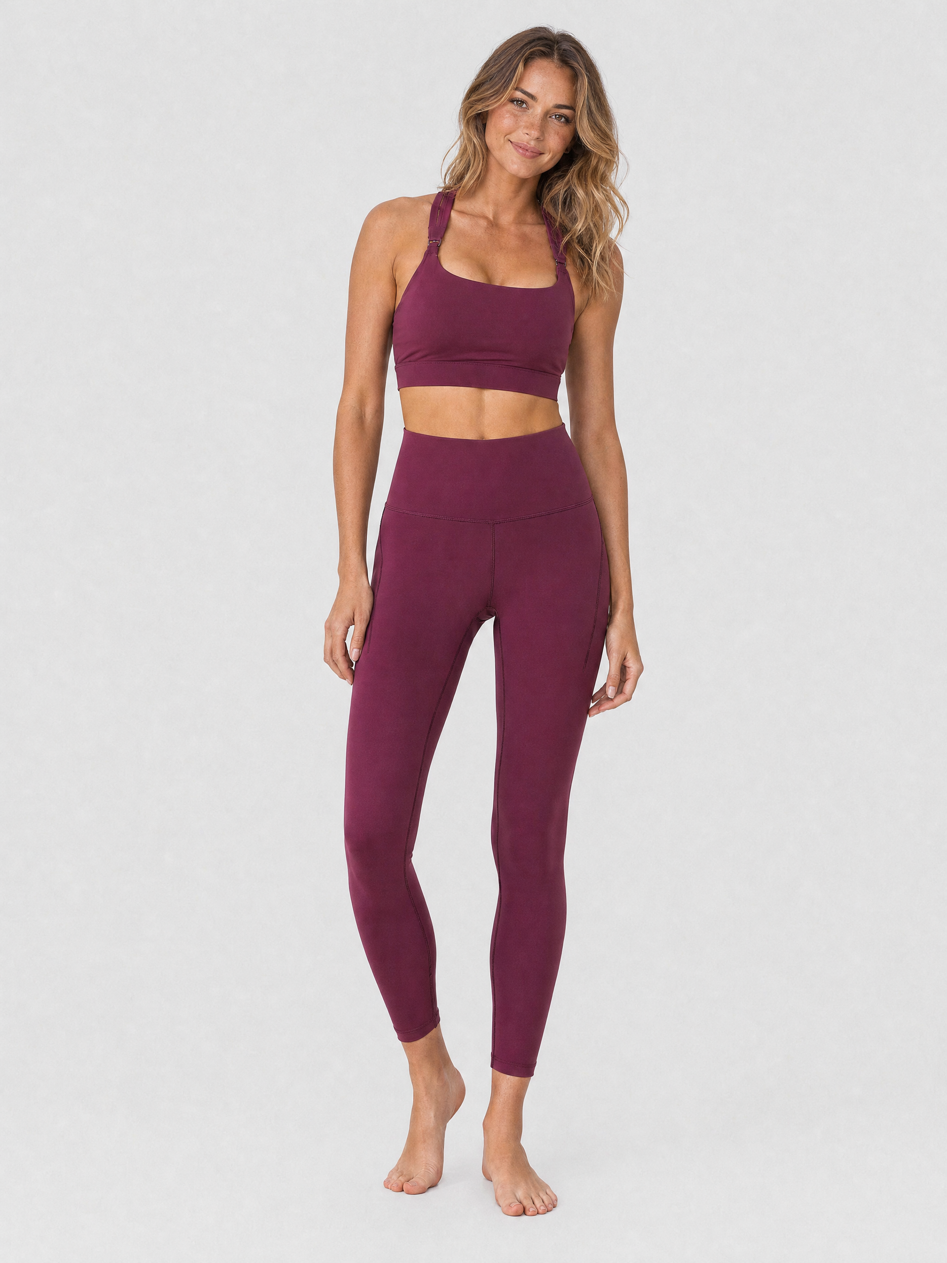 A model wearing high-waisted, full-length postpartum leggings from sweat and milk in a deep plum purple color or bordeaux color shown from the waist down against a light gray studio background, full body shot