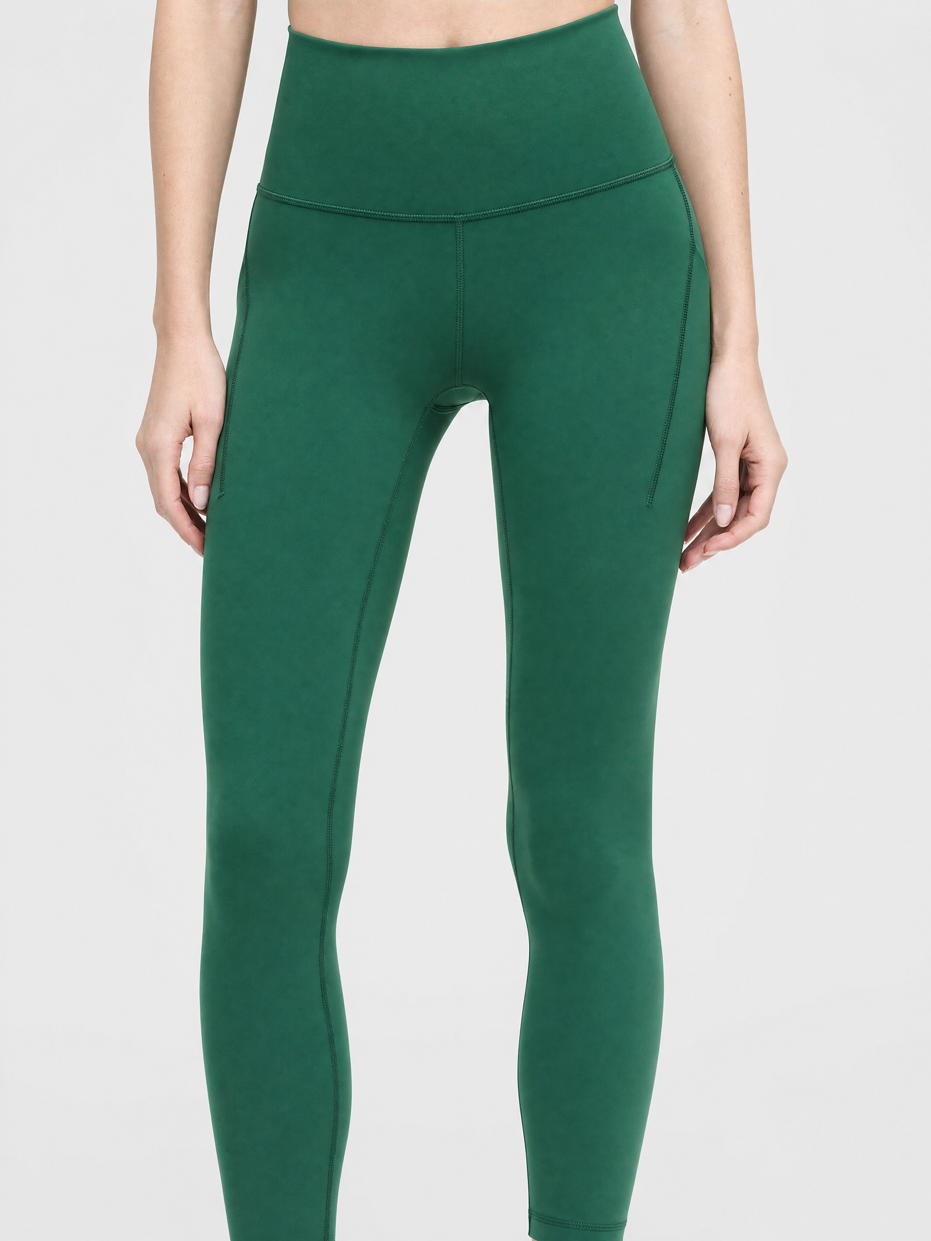 A model wearing high-waisted, full-length pine green leggings against a light gray studio background, front shot