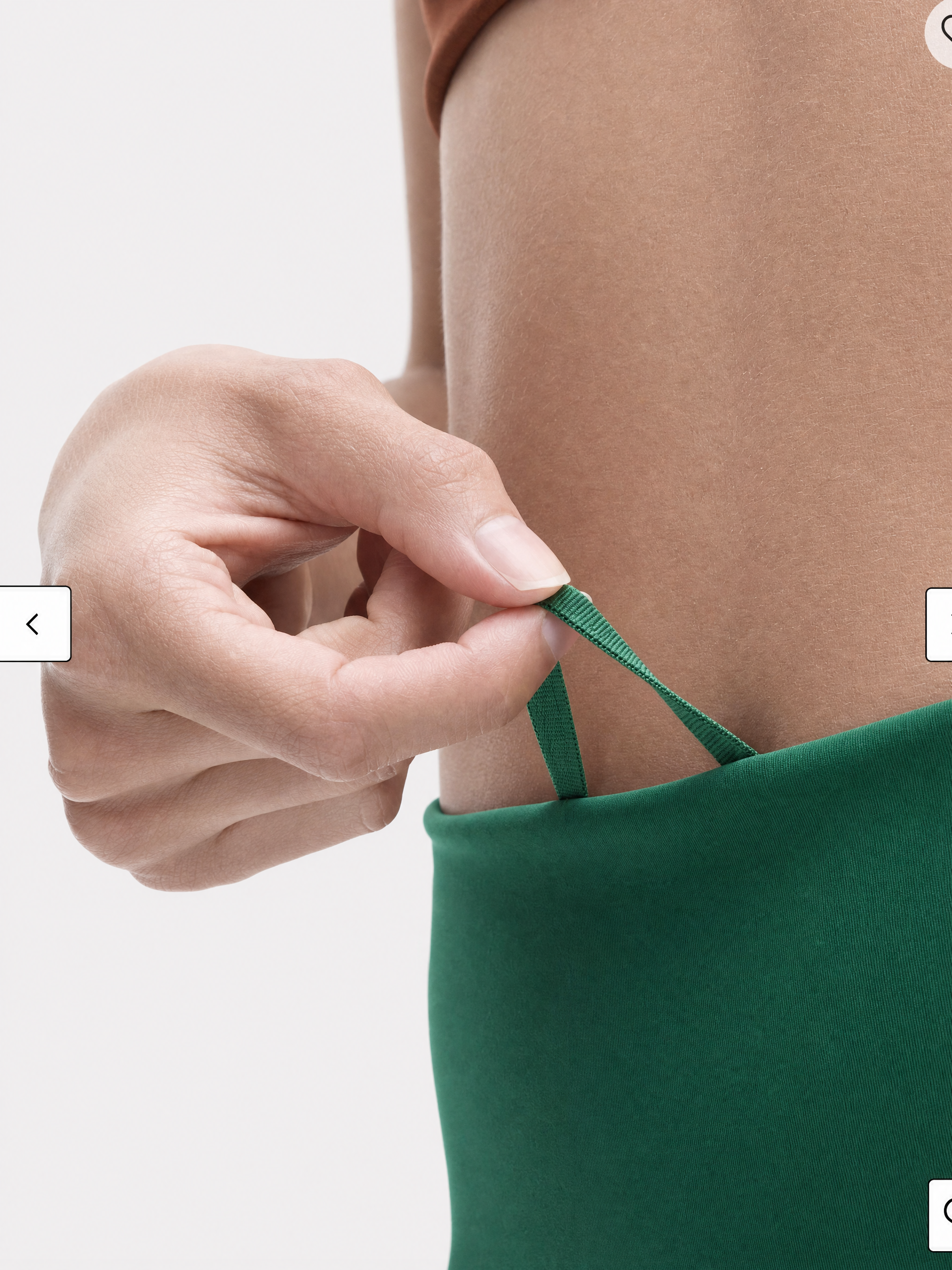 A close-up of a person's hand adjusting a green waist strap on a pine green legging's waist band, shown against a plain light gray background.